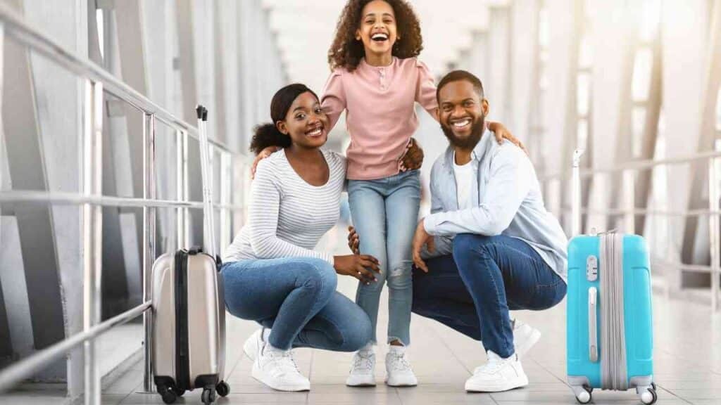 A Nigerian family smiling at the airport with luggage, ready to move abroad. 