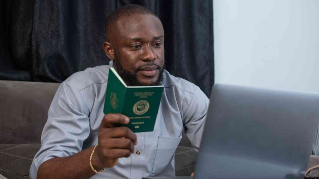 A Nigerian man holding a passport while looking at a laptop and reviewing how to leave Nigeria permanently 