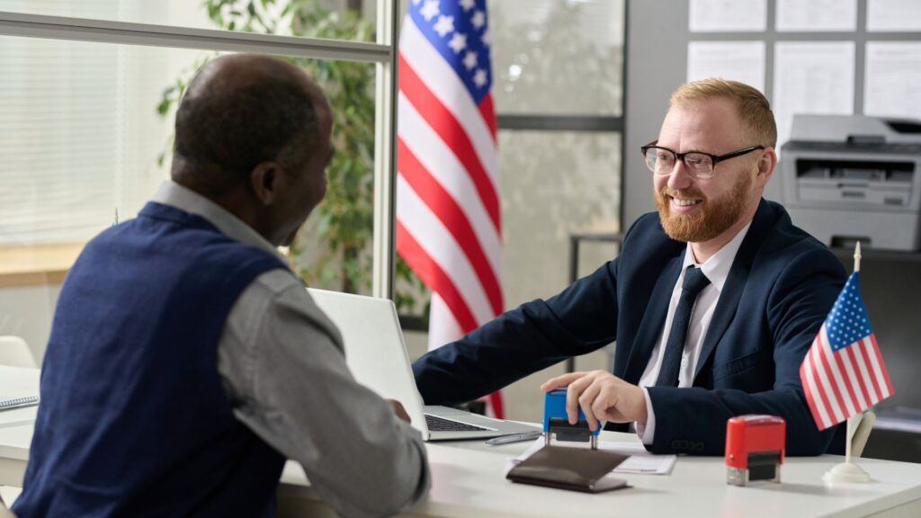 Black applicant in conversation with a US consular officer at a visa interview desk