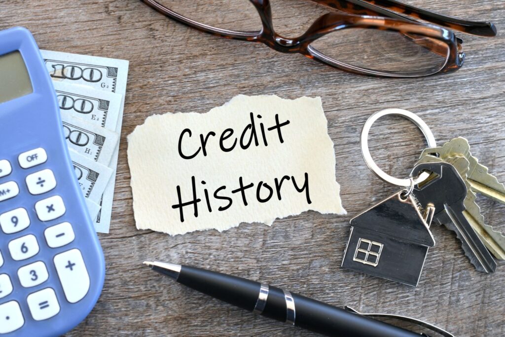 Credit history note beside US dollars, a calculator, house keys, and a pen representing financial planning for newcomers